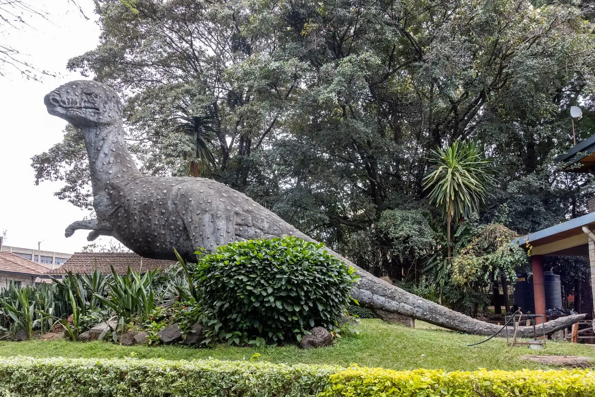 Groot dinosaurusbeeld tussen bomen en struiken in de museumtuin